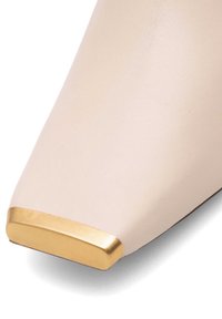 Beige ādas kurpe ar kvadrātu purngalu un zelta metālisku akcentu. Gluda tekstūra, minimālisma dizains un strukturēta forma.