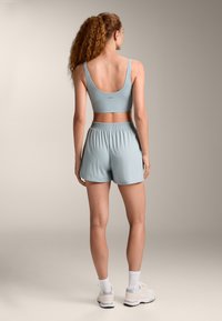 Svetlo modra športna kratka majica in hlače, izdelane iz mehkega materiala. Majica ima široke naramnice in okroglo hrbtno stran; hlače imajo elastičen pas.