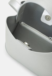 Jasnoszara torebka z otwartą górą, pokazująca wewnętrzną kieszeń na zamek oraz magnetyczne zatrzaski na jednolitym białym tle.