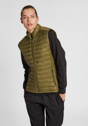 Olive green puffer vest with a high collar, zip front, and light padding. Worn over a black long-sleeve top, displayed in a neutral background.