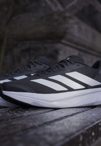 Black running shoes with white accents, featuring a lightweight mesh upper, smooth soles, and prominent three-stripe design on the sides.