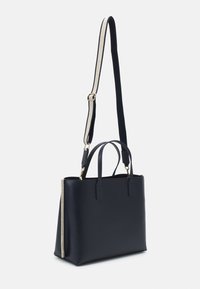 Laivastonsininen kangaskassi, joka on valmistettu sileästä synteettisestä materiaalista. Siinä on kaksi kannettavaa kahvaa, irrotettava olkahihna ja kullansävyiset metallikoristeet.