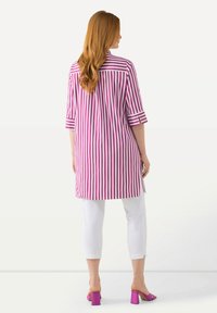 Tunica lunga a righe rosa e bianche con maniche a tre quarti, abbinata a pantaloni cropped bianchi e sandali con tacco a blocco rosa.