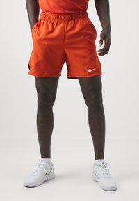 Orange Nike shorts with an elastic waistband, side pockets, and a small white logo on the hem. Smooth, lightweight fabric.