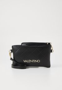 Černá prošívaná kožená spojka se zlatým logem. Obsahuje odnímatelný popruh a hladký povrch. Kompaktní obdélníkový tvar.