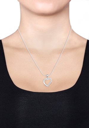 Silbernes Herzanhänger-Halsband mit funkensprühendem Rand, auf einer dünnen Kette, vor einem schwarzen Oberteil und neutralem Hintergrund präsentiert.