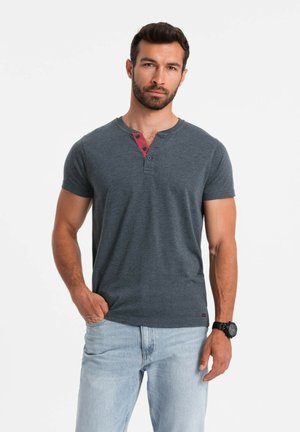 Camiseta corta de manga corta gris oscuro con cuello redondo y acentos de botones color burdeos, combinada con unos vaqueros de azul claro. Textura suave, corte casual.