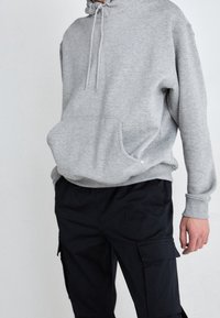 Gray hooded sweatshirt with a kangaroo pocket and drawstring closure, paired with black cargo pants featuring side pockets.