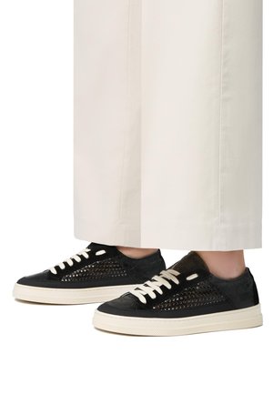 Sneakers neri con texture perforata, lacci color crema e suole in gomma bianca. Abbinati a pantaloni larghi di colore chiaro.
