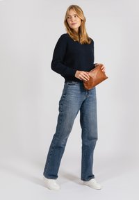 Dark navy ribbed sweater tucked into blue denim jeans. Model holds a small, brown leather clutch. White sneakers complete the outfit.