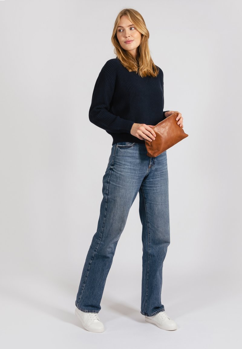 Dark navy ribbed sweater tucked into blue denim jeans. Model holds a small, brown leather clutch. White sneakers complete the outfit.