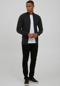 Mørkegrå zip-jakke lavet af glat stof, med høj krave. Sammen med en hvid T-shirt og sorte slim-fit bukser, afsluttet med sorte sneakers.