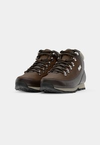 Botas de senderismo marrones con parte superior de cuero suave, ojales de metal y cordones gruesos. Suela de goma duradera con un patrón de tracción, diseño de media caña.