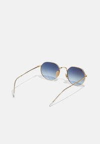 Gafas de sol ovaladas con un marco de metal dorado, lentes degradados en azul y puntas de plástico transparente en las patillas. Diseño ligero.