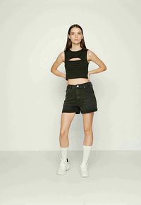 Top crop preto com um recorte frontal, combinado com calções de ganga pretos de cintura alta e meias brancas até ao joelho. Modelo a usar ténis brancos.