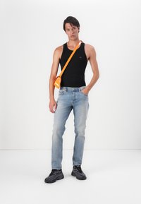 Čierny bezrukávový top, svetlomodré džínsy, čierne tenisky a malá oranžová crossbody taška. Jednoduché pozadie bez ďalších prvkov.