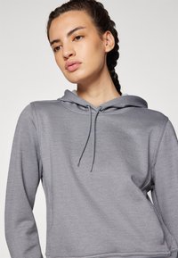 Grauer Kapuzenpullover mit schlichter Textur, verstellbarem Kordelzug und Kängurutasche. Mit einem dezenten Logo auf der Brust. Lange Ärmel.