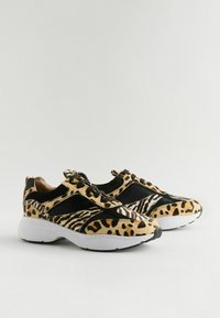 Des baskets avec un imprimé animal mixte de motifs léopard et zèbre en noir et beige, avec une semelle en caoutchouc blanche et des accents noirs.