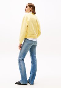 Lichtgele sweatshirt met een relaxte pasvorm, gecombineerd met lichtblauwe flared jeans. De stof lijkt zacht te zijn en de sweatshirt heeft ribgebreide manchetten.