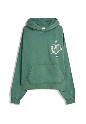 Sweatshirt à capuche vert avec poche avant, portant le texte blanc "Les cœurs ne mentent pas" et un motif d'étoile. Tissu doux avec une coupe décontractée.