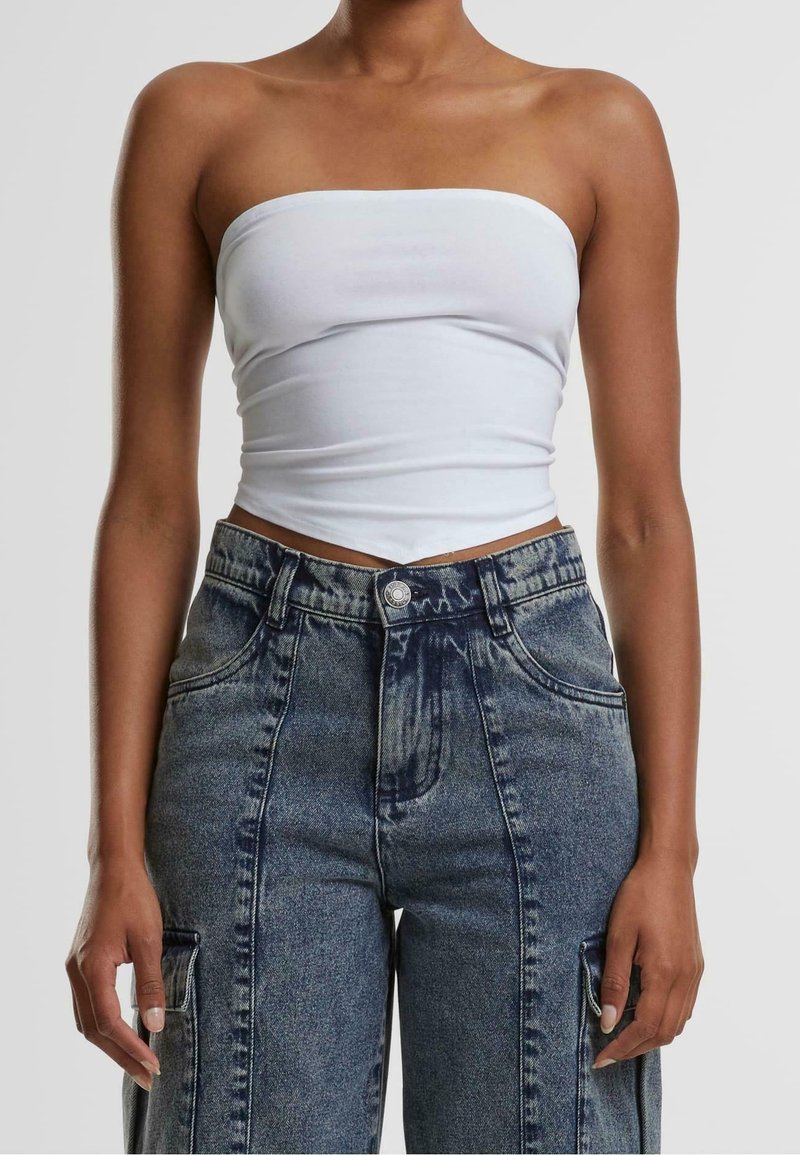 Femme portant un crop top blanc sans bretelles et un jean bleu taille haute avec des poches devant et des poches cargo sur les cuisses.
