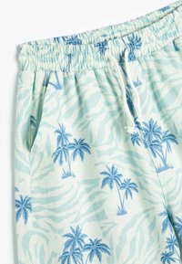 Lyseblå shorts med palmetræ- og zebrastribet mønster. Fremstillet af blødt materiale, med elastisk talje og snor.