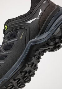Cizme negre de drumeție cu uppere texturate din GORE-TEX, accente reflective și o talpă din cauciuc rugged cu bulduri proeminente pentru tracțiune.