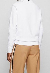 Vit sweatshirt med långa ärmar, ribbad mudd och nederkant, bärs med beige byxor med svartvita sidosträck. Minimalistisk design.