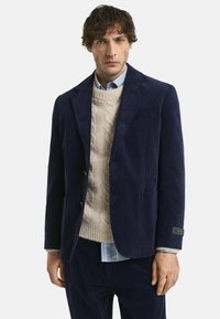 Marineblauer Cordblazer mit zwei Hosentaschen und goldfarbenen Beschl�ägen, kombiniert mit einem cremefarbenen Grobstrickpullover und einem hellblauen Hemd.