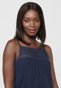 Haut sans manches bleu marine avec des détails en dentelle complexes au niveau du col. Matière légère, coupe ample et texture douce.