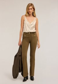 Camisole din satin bej deschis cu un design pliat, asortat cu blugi evazați de culoare verde măslin, ce au buzunare frontale și nasturi de culoare aurie. Botine negre cu toc.
