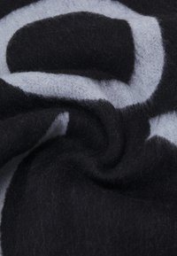 Minkštas vilnos ir sintetinių pluoštų audinys, turintis juodą ir šviesiai pilką abstraktų raštą. Tinkama tekstūra yra pūkuota, su jaukiu, megztu išvaizda.