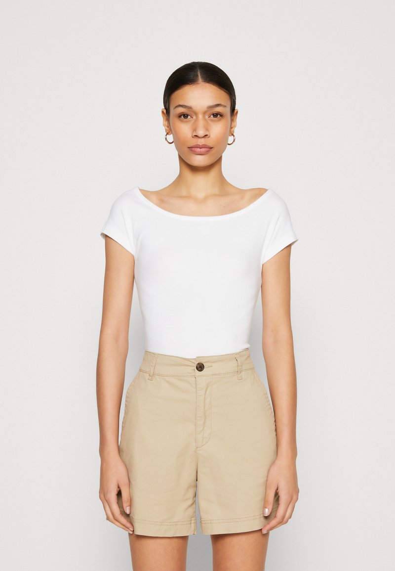 White short-sleeve top with a wide neckline paired with beige shorts, featuring a button closure and a relaxed fit. Smooth texture throughout.