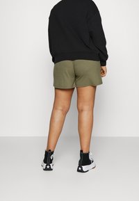 Shorts côtelés vert olive avec une coupe décontractée, associés à un sweat noir et des baskets montantes noires avec des accents blancs.