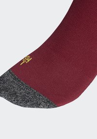 Burgundské ponožky s textúrovanou tkaninou, šedým melírovaným manžetom a žltým logom. Obsahujú zosilnené špičky a päty pre väčšiu trvácnosť.