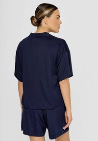 Marineblaue Sportbekleidung bestehend aus einem locker sitzenden kurzärmligen Oberteil und passenden Shorts, gefertigt aus leichtem Material mit glatter Textur.