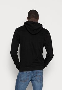 Sort hættekartot med lange ærmer, ribbede manchetter og en kengurulomme. Båret med blå denimjeans, der har en klassisk pasform.