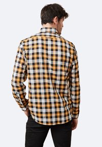 Camisa de cuadros para hombre en negro, blanco y naranja. Tejido de algodón, mangas largas, cuello abotonado y dobladillo redondeado. Costuras laterales visibles.