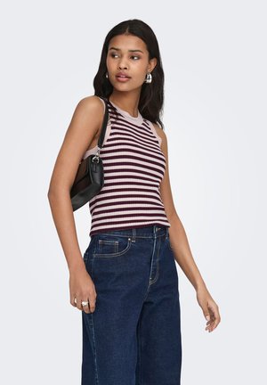Jeune femme portant un haut sans manches rayé, un jean bleu, des boucles d'oreilles anneaux argentées et un petit sac noir à l'épaule.