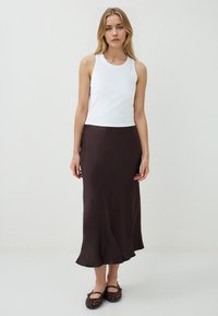 Top sans manches blanc associé à une jupe midi en satin marron, avec un ourlet évasé et une texture lisse. Porté avec des ballerines tressées marron.