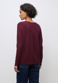 Burgunderfarbener Pullover mit langen Ärmeln, weitem Rundhalsausschnitt und weicher Textur, kombiniert mit dunkelblauen weiten Jeans.
