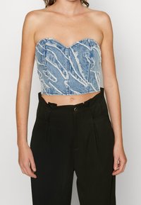 Denimová bandeau top s vyztuženým tvarem, vyrobená ze světle modrého materiálu, s třepenými detaily a jemným bílým prošitím.