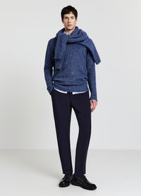 Pull en tricot bleu marine avec un col roulé, assorti à une chemise bleu clair et un pantalon foncé taillé sur mesure. Des chaussures noires complètent la tenue.