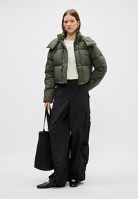 Doudoune verte avec un design court et un grand col, associée à un pantalon cargo noir ample et un sac fourre-tout noir. Chaussures noires avec clous.
