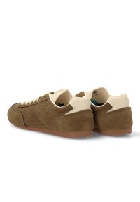 Zapatillas de gamuza marrón con acentos beige, que cuentan con una superficie texturizada, punta redonda y suela de goma. Los cordones y la marca son visibles en la lengüeta.