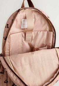 Open pink quilted backpack with brown cherry pattern, showing inner padded laptop sleeve and name label inside.