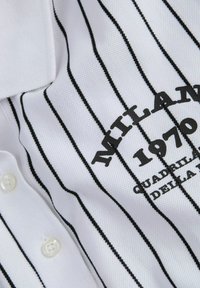 Chemise polo blanche avec des rayures verticales noires, dotée d'un col boutonné et du texte brodé "MILAN 1970", en tissu texturé.