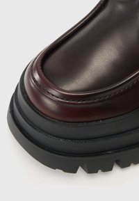 Pruuni nahkjalanõud läikiva viimistlusega, ümar varvas, silmapaistev õmblemine ja paks must kummitald, millel on mustri jälg.