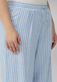 Lichtblauwe gestreepte broek van zacht materiaal, met verticale witte strepen, een trekkoord in de taille en zijplooien voor extra detail.