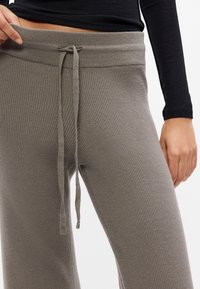 Sive rebraste trenirke s pojasom na vezanje. Tkanina ima teksturiranu površinu koja naglašava elastični pojas i opušteni kroj.